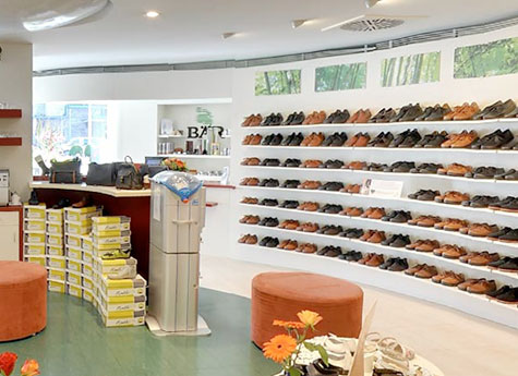 Innenansicht eines Schuhgeschäfts mit Regalen voller Herrenschuhe und einer gemütlichen Sitzecke