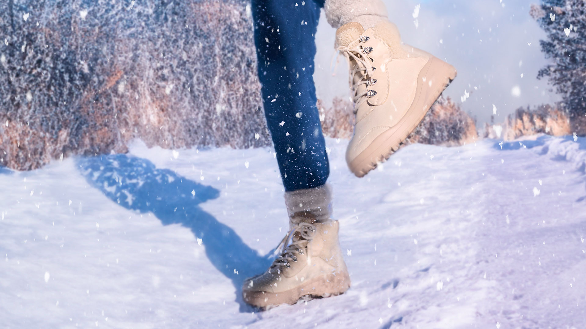 Nahaufnahme von beige Winterstiefeln, die durch eine verschneite Landschaft gehen