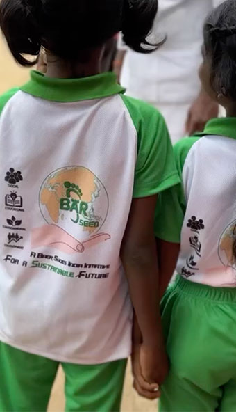 Zwei Kinder in grünen und weißen Schuluniformen mit einem Logo und dem Text 'For a Sustainable Future' auf dem Rücken.