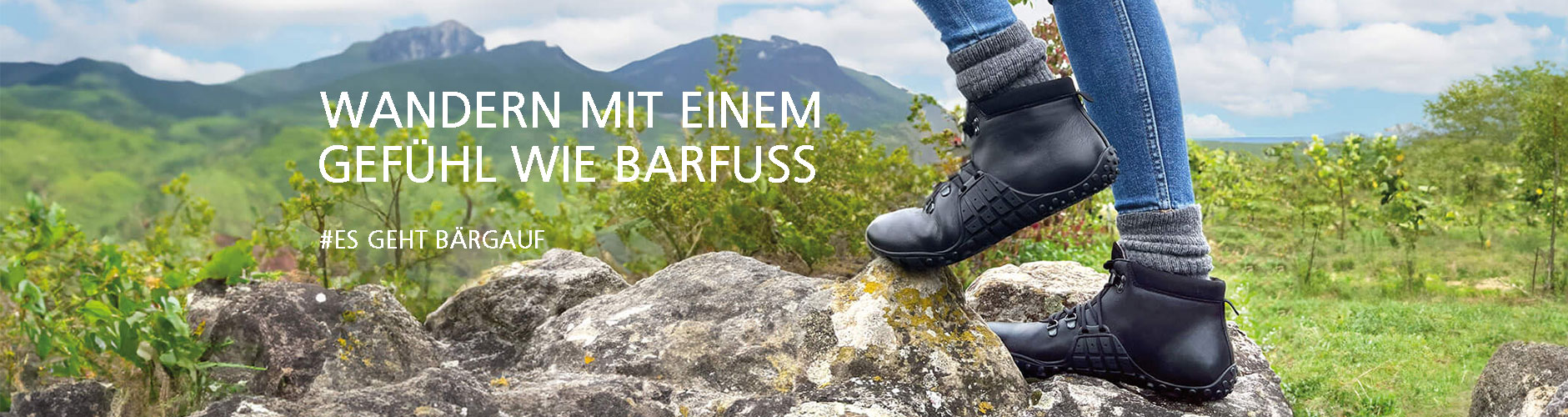 Person in Wanderschuhen auf einem Felsen mit Berglandschaft im Hintergrund