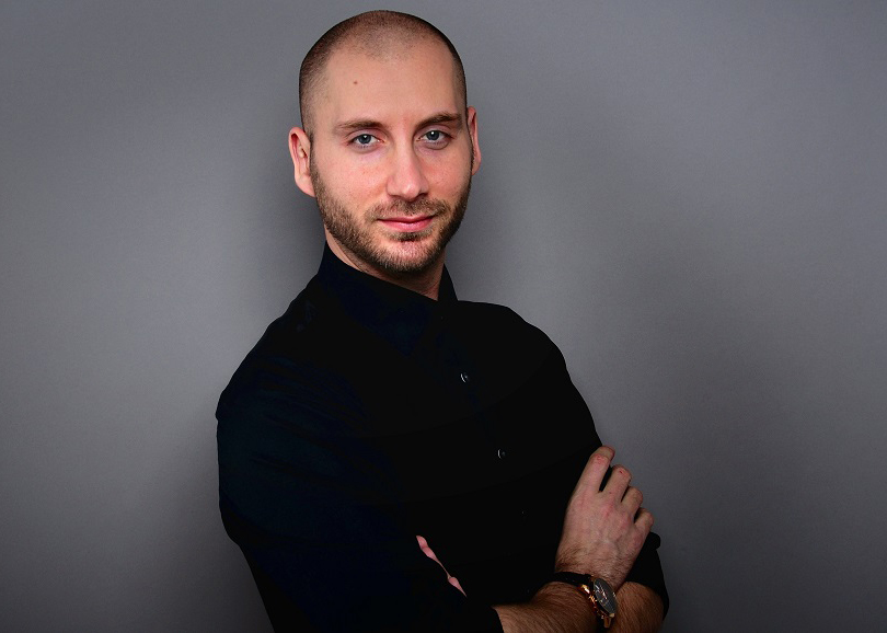 Mann mit Glatze und Bart in schwarzem Hemd, grauer Hintergrund