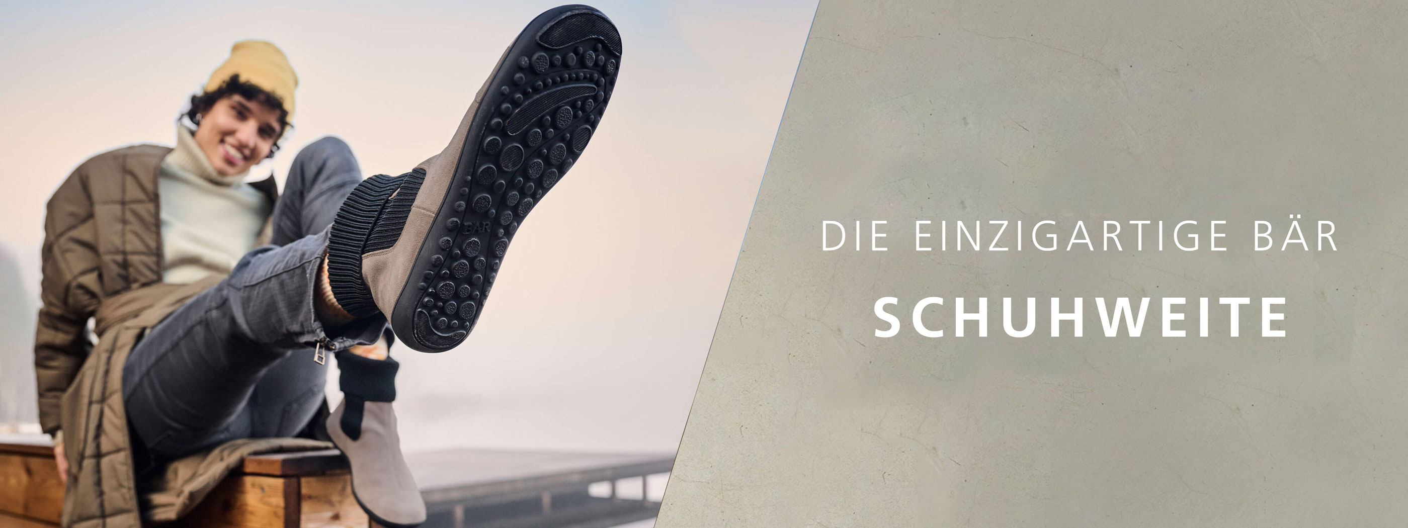 Ein Mann sitzt entspannt und hebt den Fuß mit einem Schuh, der eine besondere Bär-Schuhweite hat und eine rutschfeste Sohle zeigt.