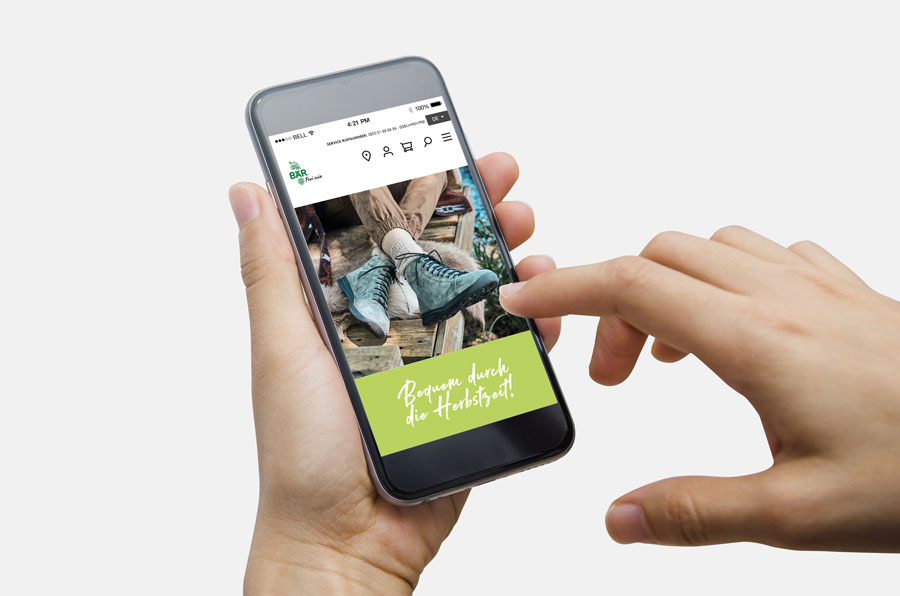 Hand hält Smartphone mit Onlineshop für Schuhe auf dem Bildschirm