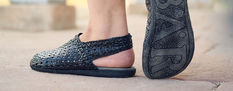 Nahaufnahme von Füßen in handgefertigten, geflochtenen Slippern auf Steinboden