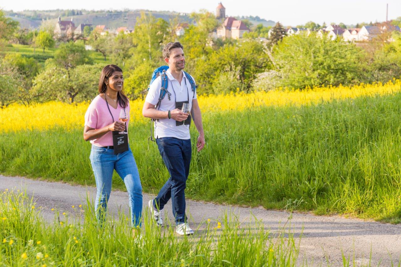 Ein Mann und eine Frau spazieren in einer grünen Landschaft und halten Gläser mit Getränken in der Hand
