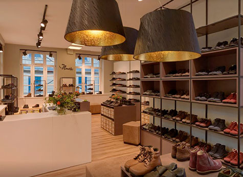 Innenansicht eines modernen Schuhgeschäfts mit Pflanzen, Regalen voller Schuhe und großer Beleuchtung.