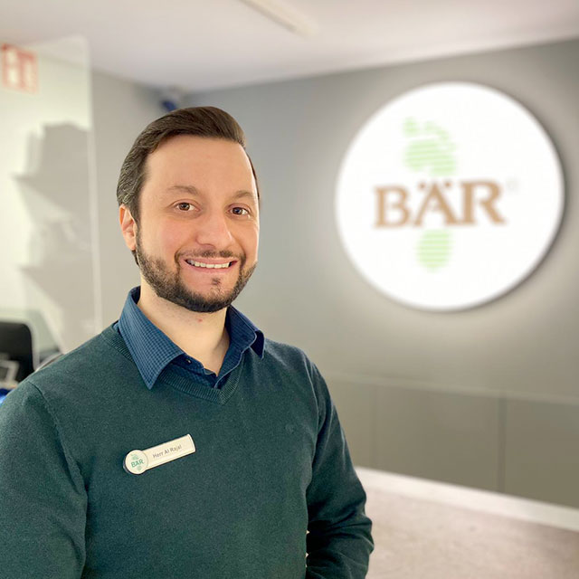 Ein Mann lächelt in einem BÄR-Schuhgeschäft mit einem Namensschild an seiner Kleidung.