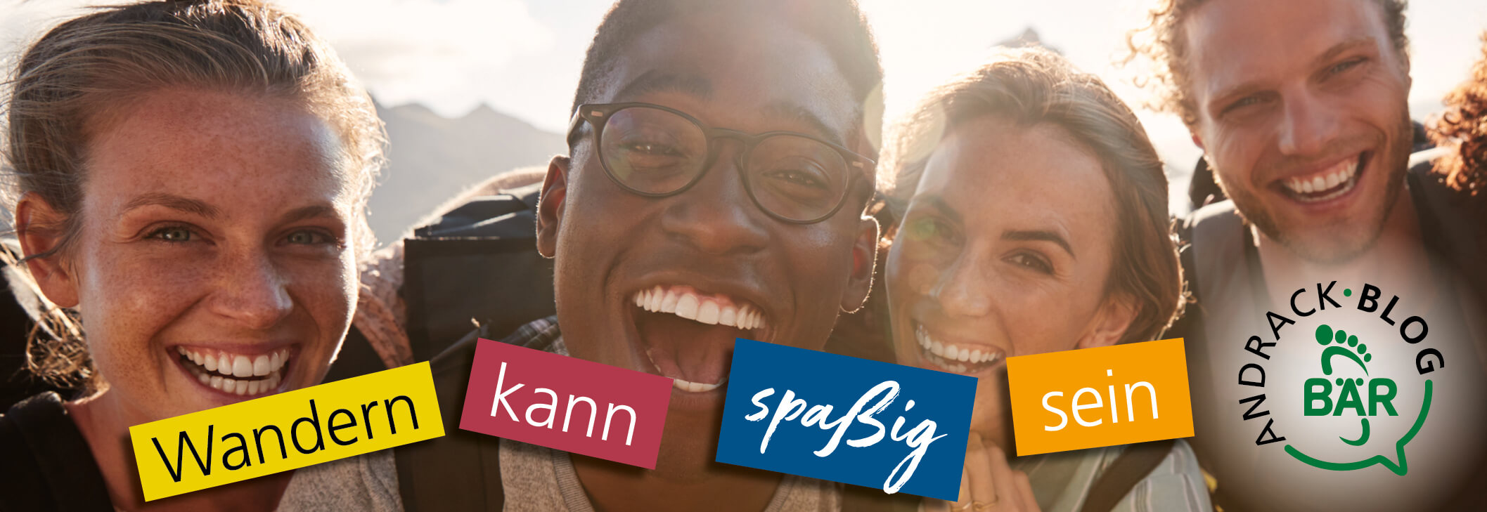 Vier fröhliche Wanderer lächeln in die Kamera, während sie die Natur genießen. Text auf dem Bild: 'Wandern kann spaßig sein'. Andrack-Blog Logo sichtbar.