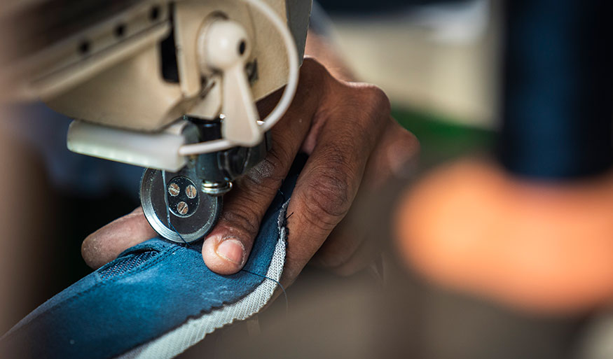 Eine Person näht einen Stoff mit einer Nähmaschine, Nahaufnahme der Hand und des Stoffes.