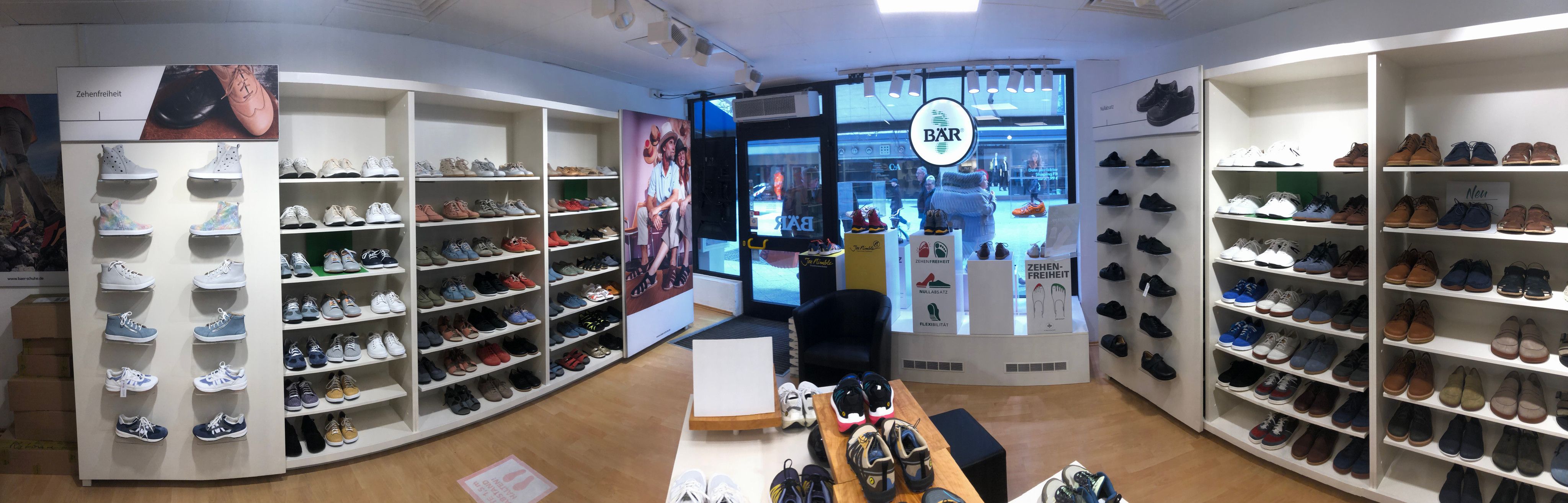 Innenansicht eines modernen Schuhladens mit diversen Sneakern und Lederschuhen in Regalen, samt ‚Zehenfreiheit‘-Plakat an der Wand