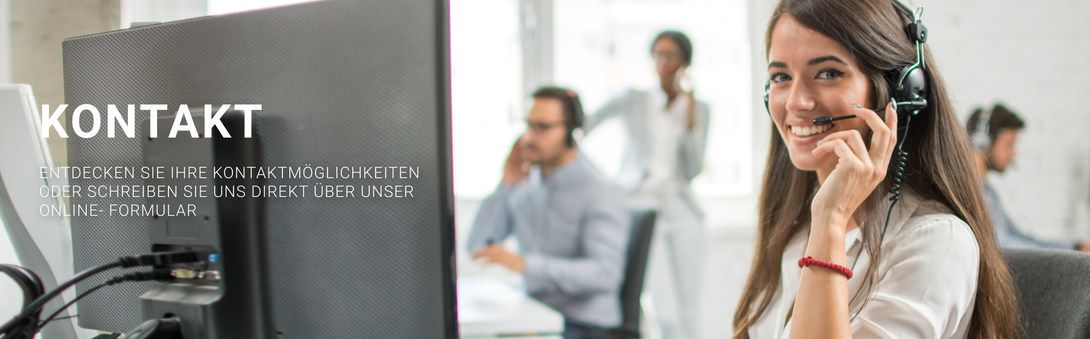 Junge Frau mit Headset lächelnd am Schreibtisch, Kollegen im Hintergrund