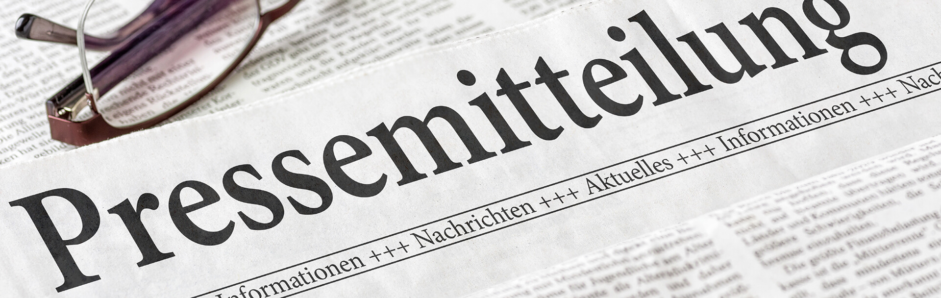 Nahaufnahme einer Zeitung mit der Überschrift 'Pressemitteilung' und einer Brille darauf