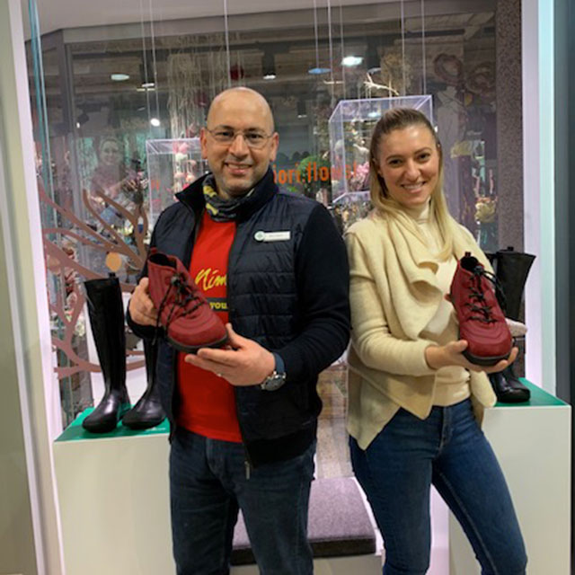 Zwei Personen halten rote Schuhe vor einem Schaufenster mit weiteren Stiefeln