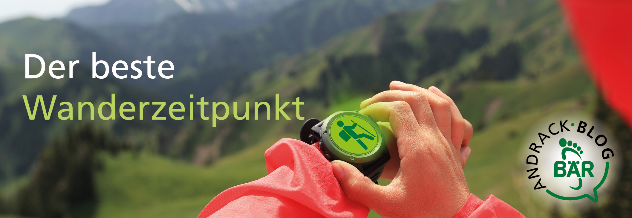 Nahaufnahme einer Hand, die eine grüne Smartwatch mit Wander-Symbol hält, im Hintergrund unscharfe Berglandschaft und Andrack Blog Bär Logo