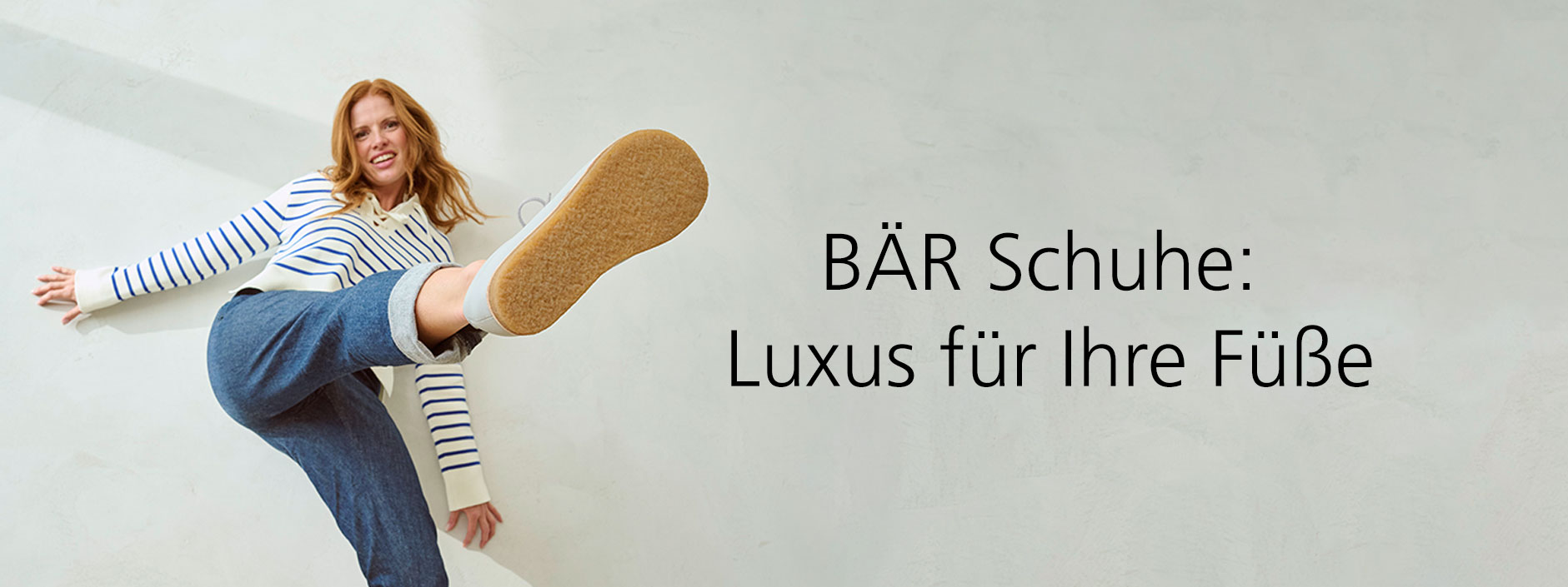 Eine Frau in lässiger Kleidung präsentiert ein Paar bequemer BÄR Schuhe mit großer Begeisterung.